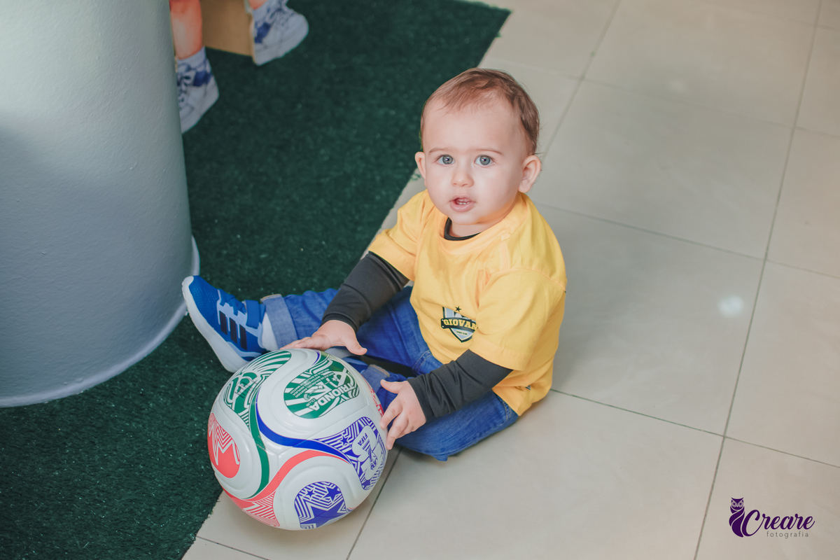 Uma criança sentada no chão brincando com uma bola, durante seu aniversário de 1 ano.