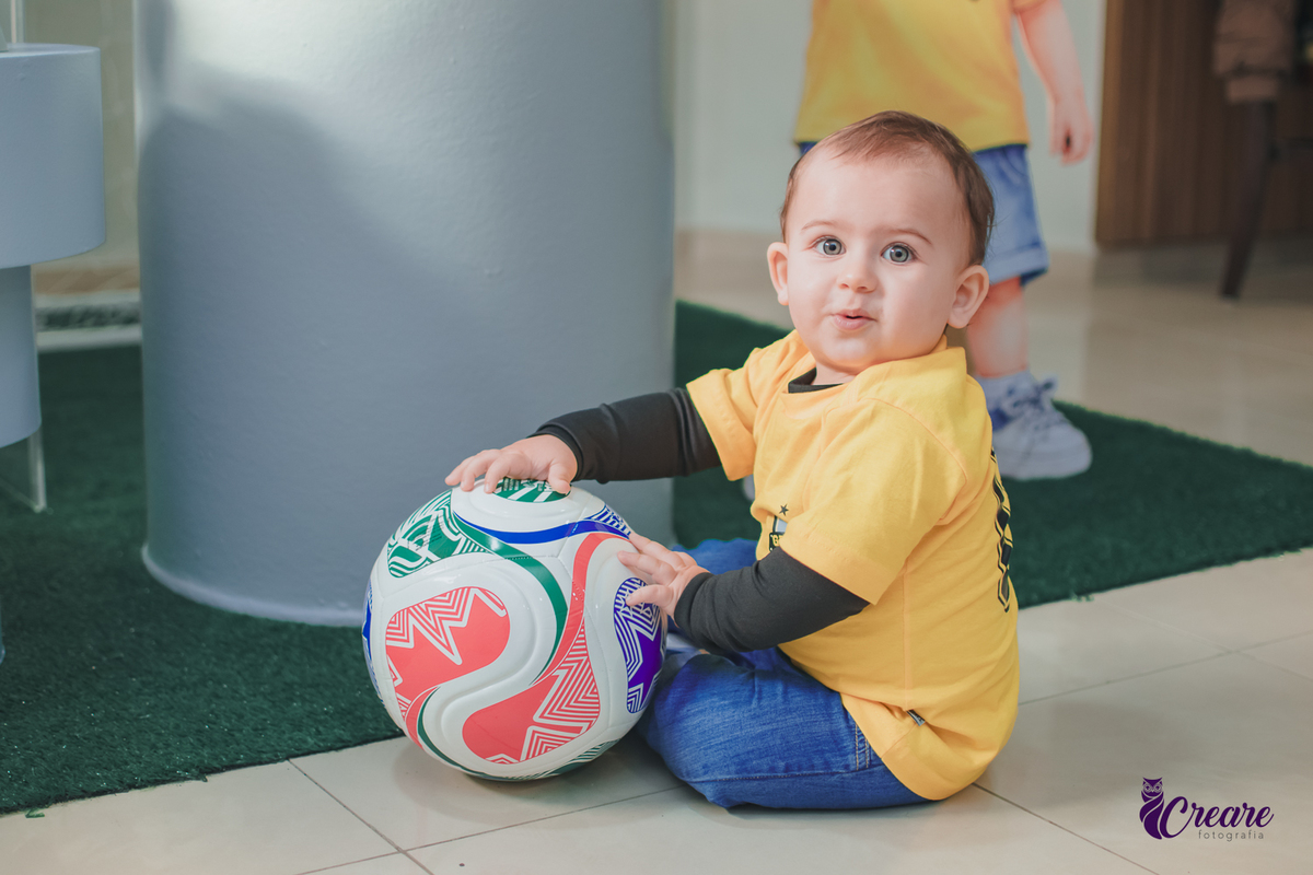 Uma criança sentada no chão brincando com uma bola, durante seu aniversário de 1 ano.