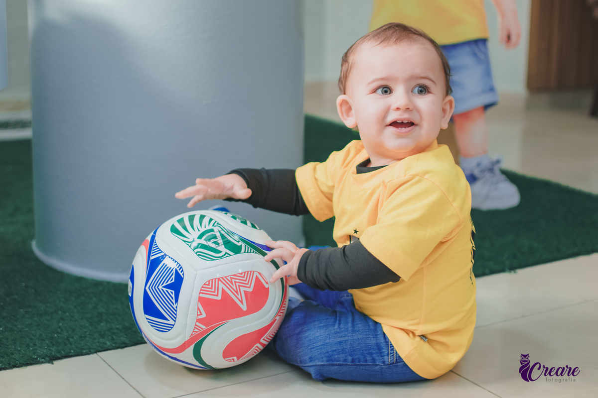 Uma criança sentada no chão brincando com uma bola, durante seu aniversário de 1 ano.