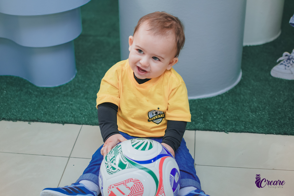 Uma criança sentada no chão brincando com uma bola, durante seu aniversário de 1 ano.
