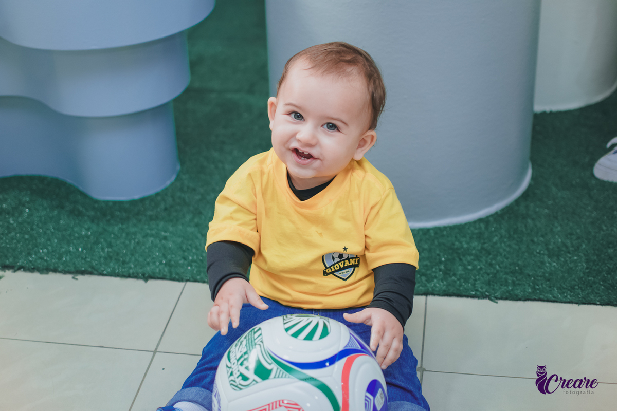 Uma criança sentada no chão brincando com uma bola, durante seu aniversário de 1 ano.