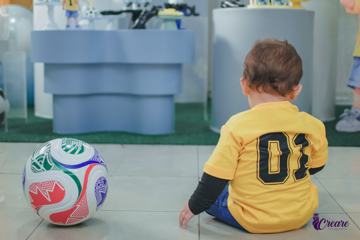 Uma criança sentada no chão brincando com uma bola, durante seu aniversário de 1 ano.