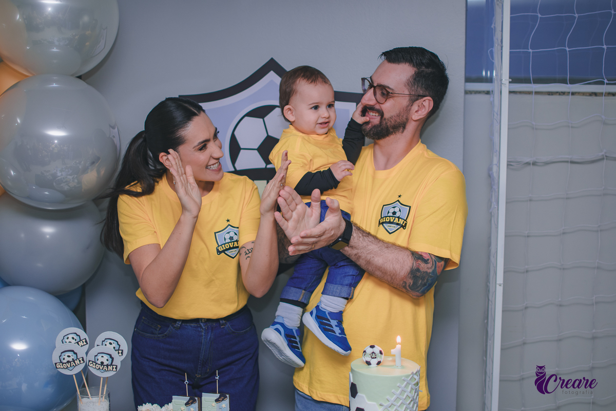 Família canta parabéns para um bebê de 1 ano durante a festa de aniversário, reunida ao redor da mesa de decoração em um momento de celebração.