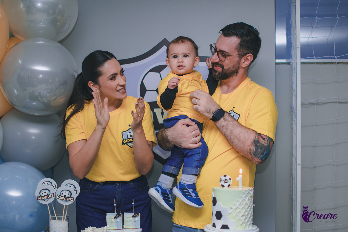Família canta parabéns para um bebê de 1 ano durante a festa de aniversário, reunida ao redor da mesa de decoração em um momento de celebração.