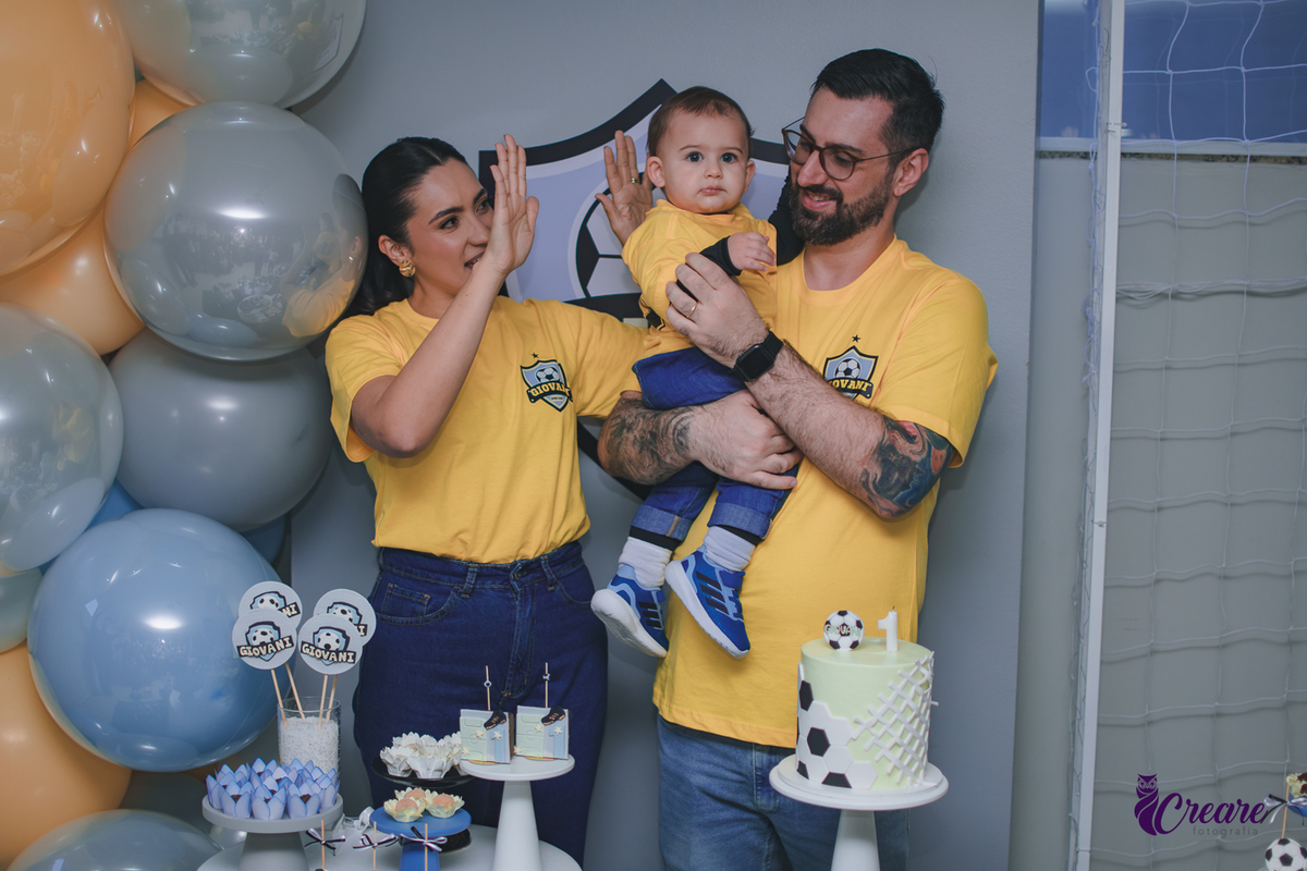 Família canta parabéns para um bebê de 1 ano durante a festa de aniversário, reunida ao redor da mesa de decoração em um momento de celebração.