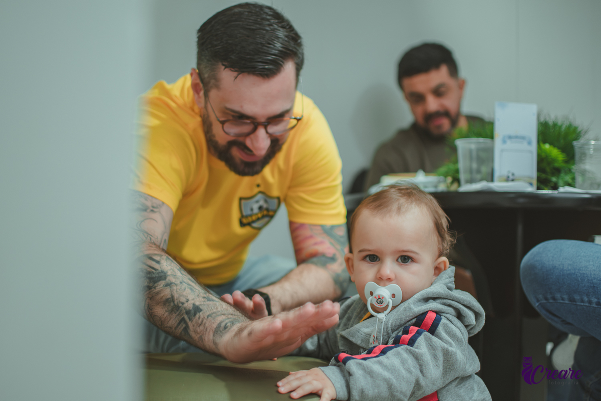 Bebê brincando com seu pai em uma cadeira, durante sua festa de aniversário de 1 ano.