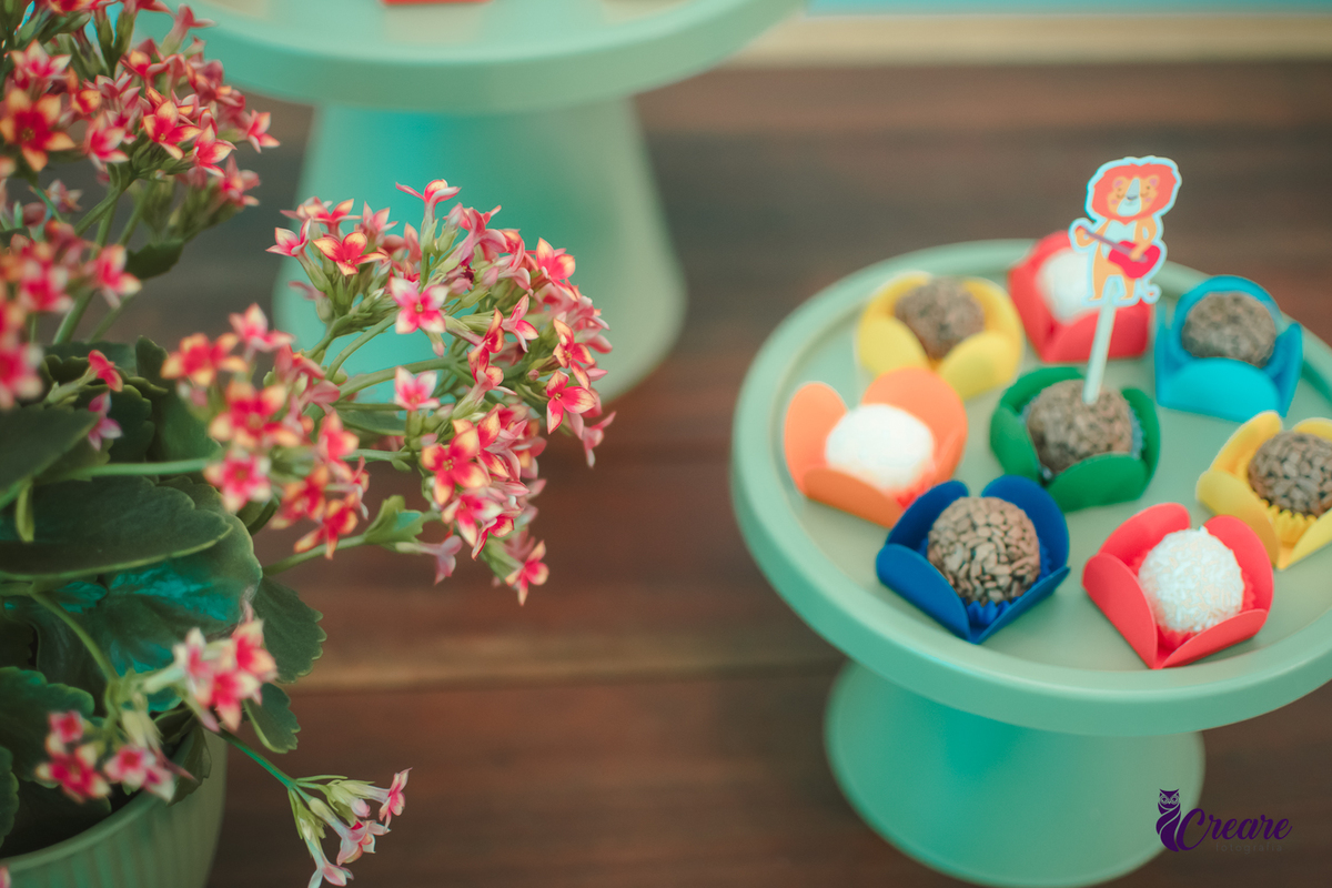 docinhos de festa decorado com o tema banda dos animais, ao lado de uma vaso de flores vermelhas.