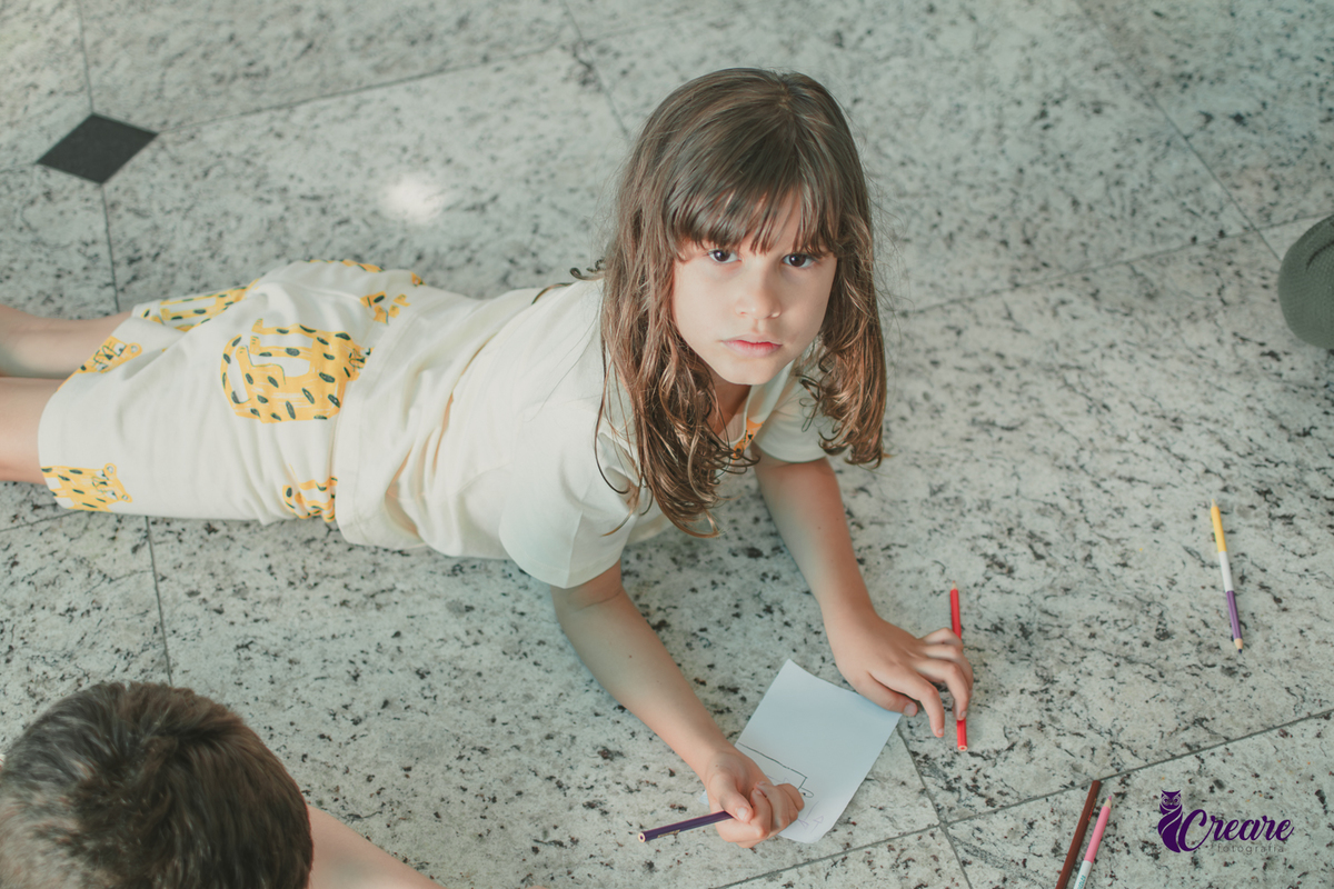 Uma criança desenhando no chão, durante festa de aniversário infantil em casa.