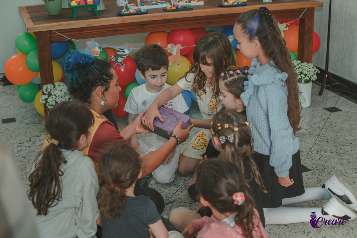 Crinaças, reunidas no chão, brincando durante festa de aniversário infantil.