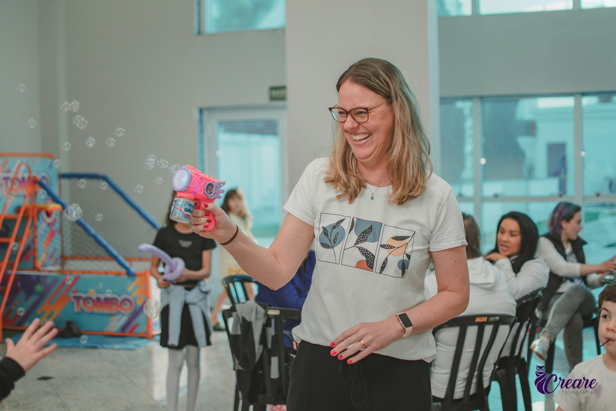 Uma mulher jogando bolhas de sabão paraa crianças durante uma festa de aniversário infantil.