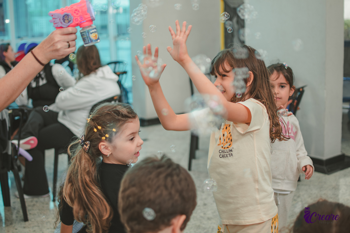 Crianças brincando com bolha de sabão, durante festa de aniversário infantil.