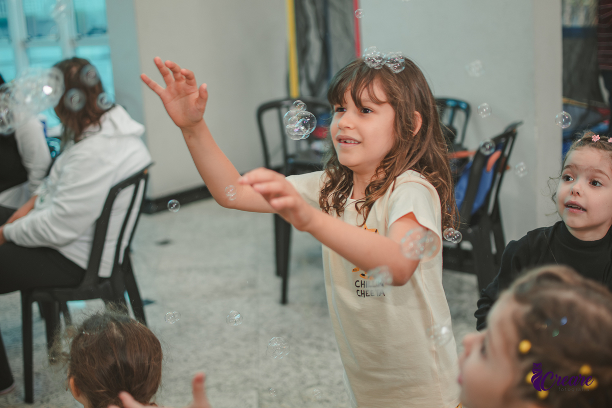 Crianças brincando com bolha de sabão, durante festa de aniversário infantil.