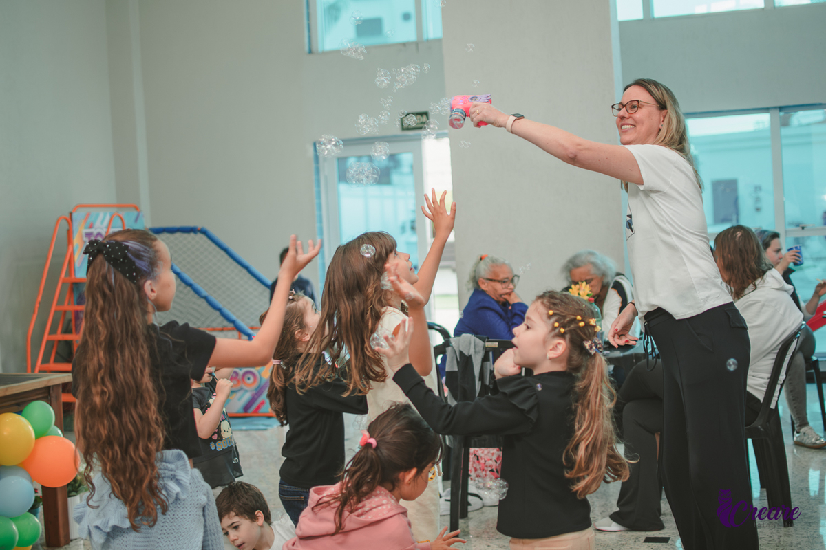 Uma mulher jogando bolhas de sabão paraa crianças durante uma festa de aniversário infantil.