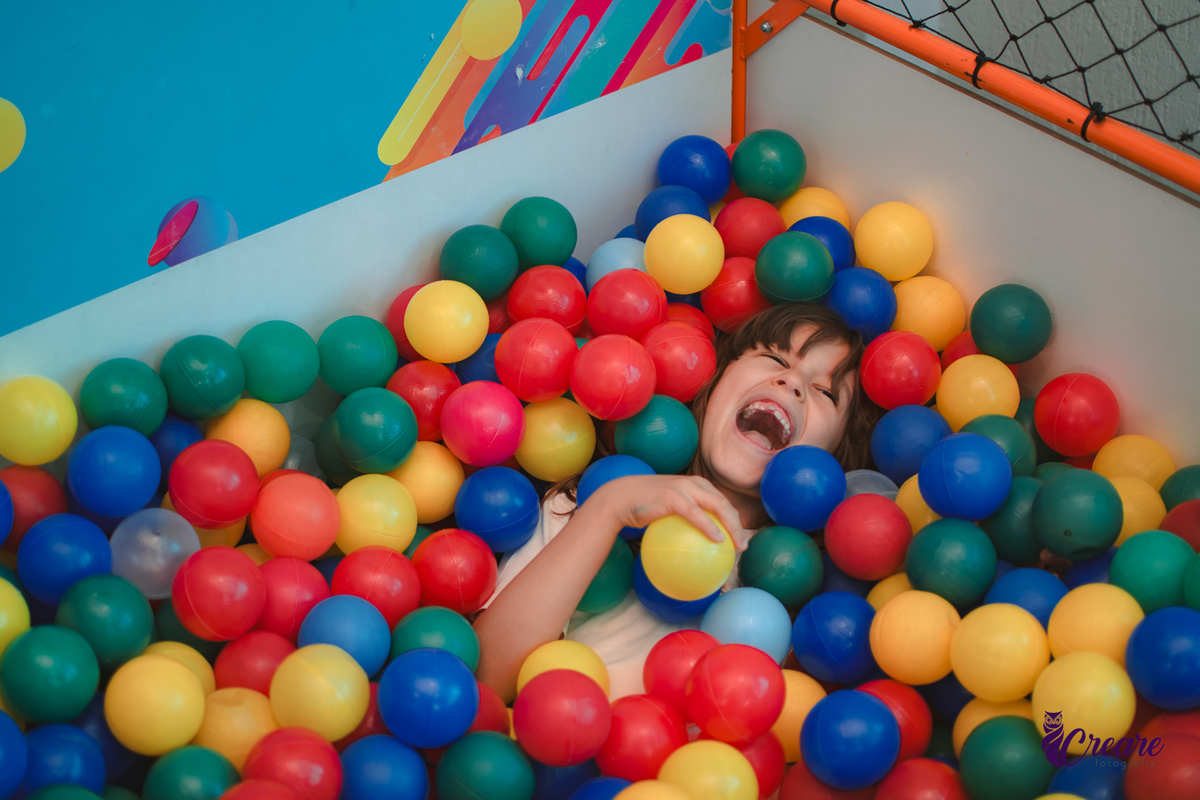Um menino sorrindo dentro de uma piscina de bolinhas, durante sua festa de aniversário em casa.