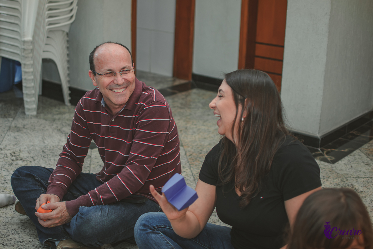 Um homem e uma mulher, sorrindo, durante brincadeira musical em festa infantil.