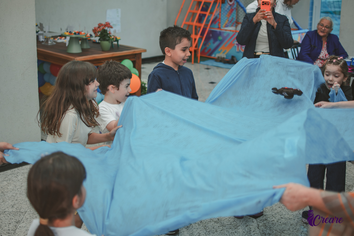 Crinaças brincando de sacudir tecido azul, durante brincadeira de aniversário infantil.