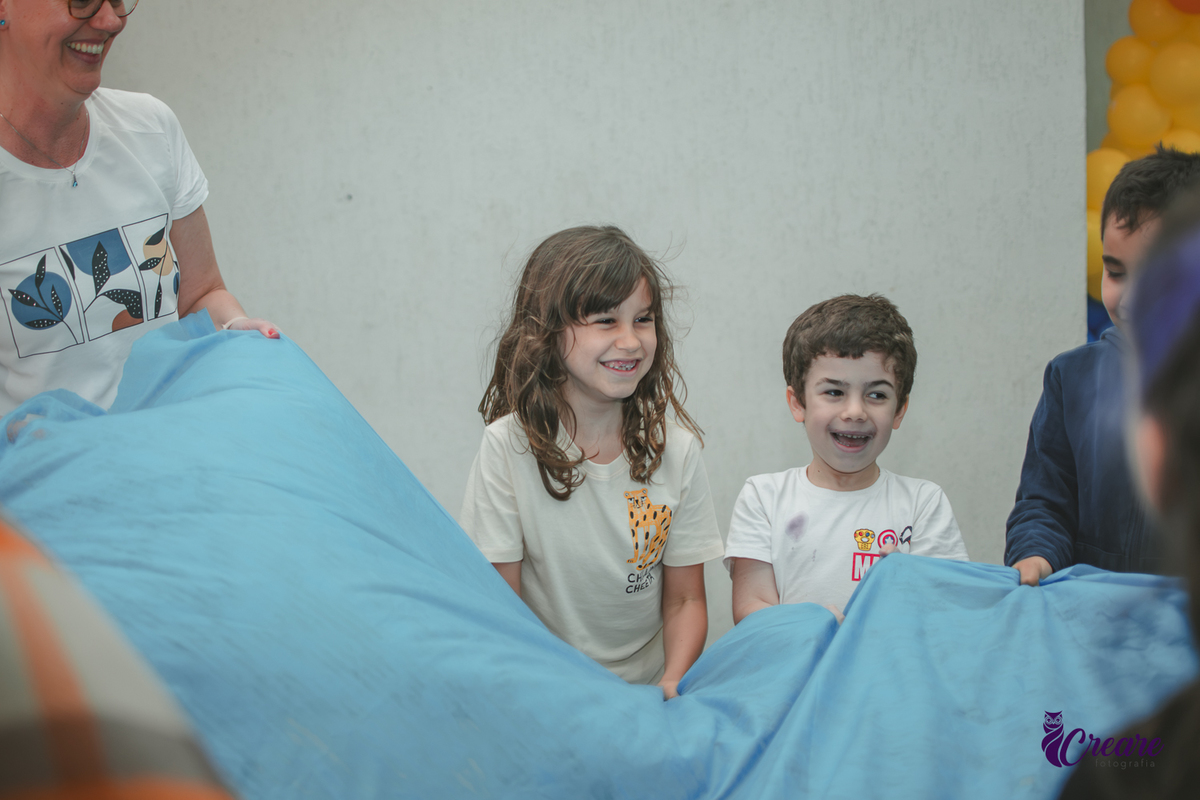 Crinaças brincando de sacudir tecido azul, durante brincadeira de aniversário infantil.