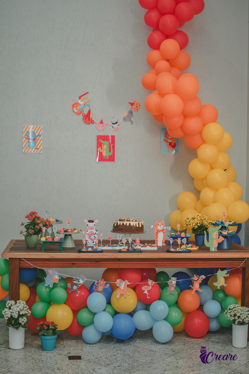 Decoração de festa infantil em casa com tema Banda dos Bichos, mesa colorida com balões, bolo e doces personalizados para aniversário de 7 anos.