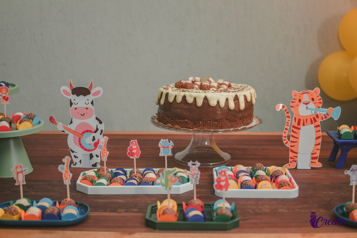 Decoração de festa infantil em casa com tema Banda dos Bichos, mesa colorida com balões, bolo e doces personalizados para aniversário de 7 anos.