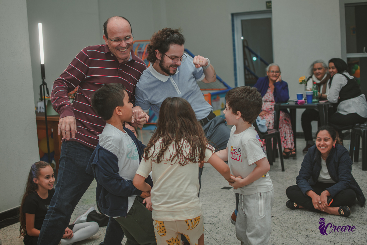 Dois adultos e várias crianças brincando de dançar, durante festa de aniversário infantil em casa.