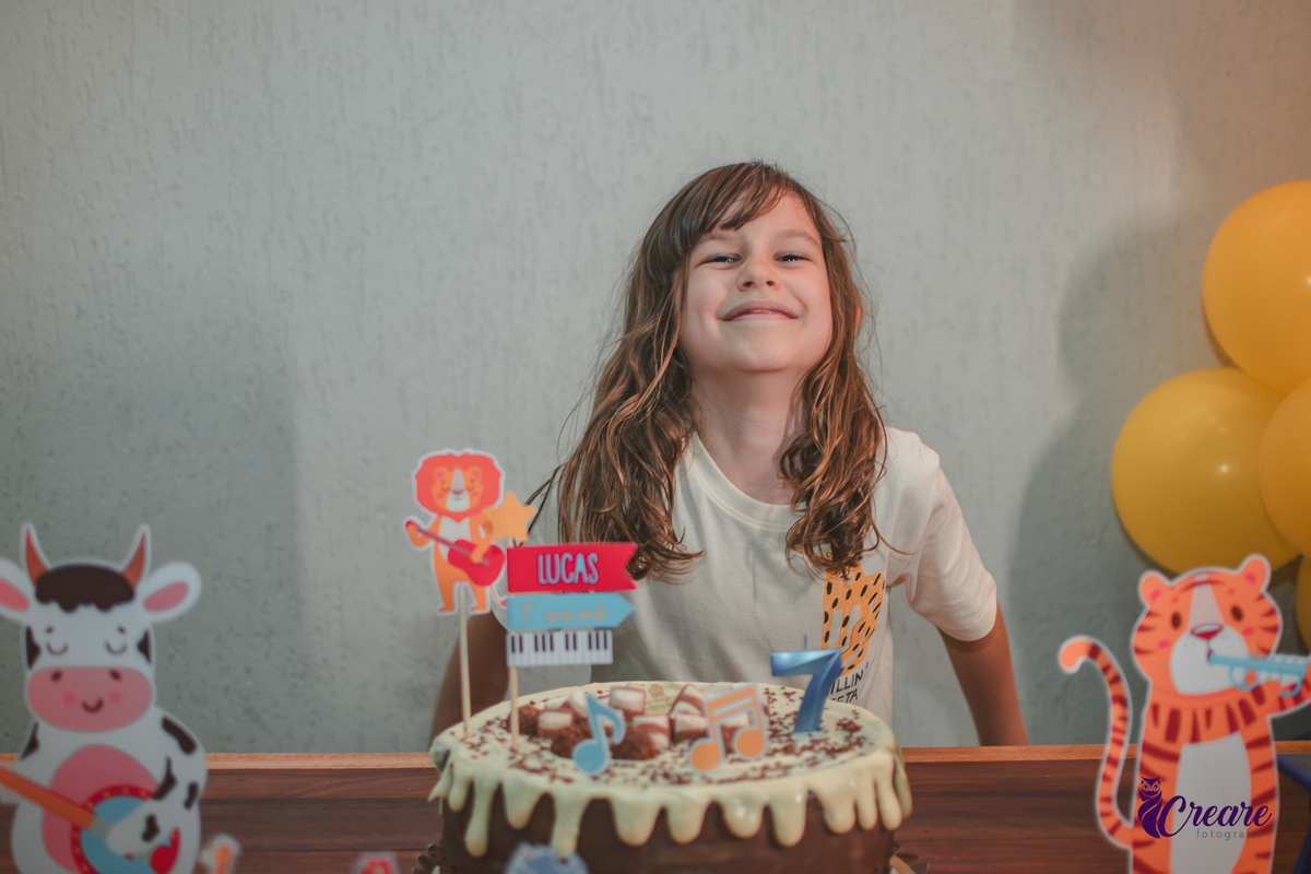 Uma crianças sorrindo em frente ao seu bolo de aniversário.