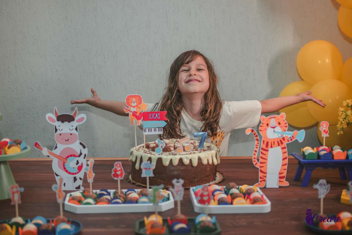 Uma crianças, sorrindo de braços abertos, em frente seu bolo de aniversário.