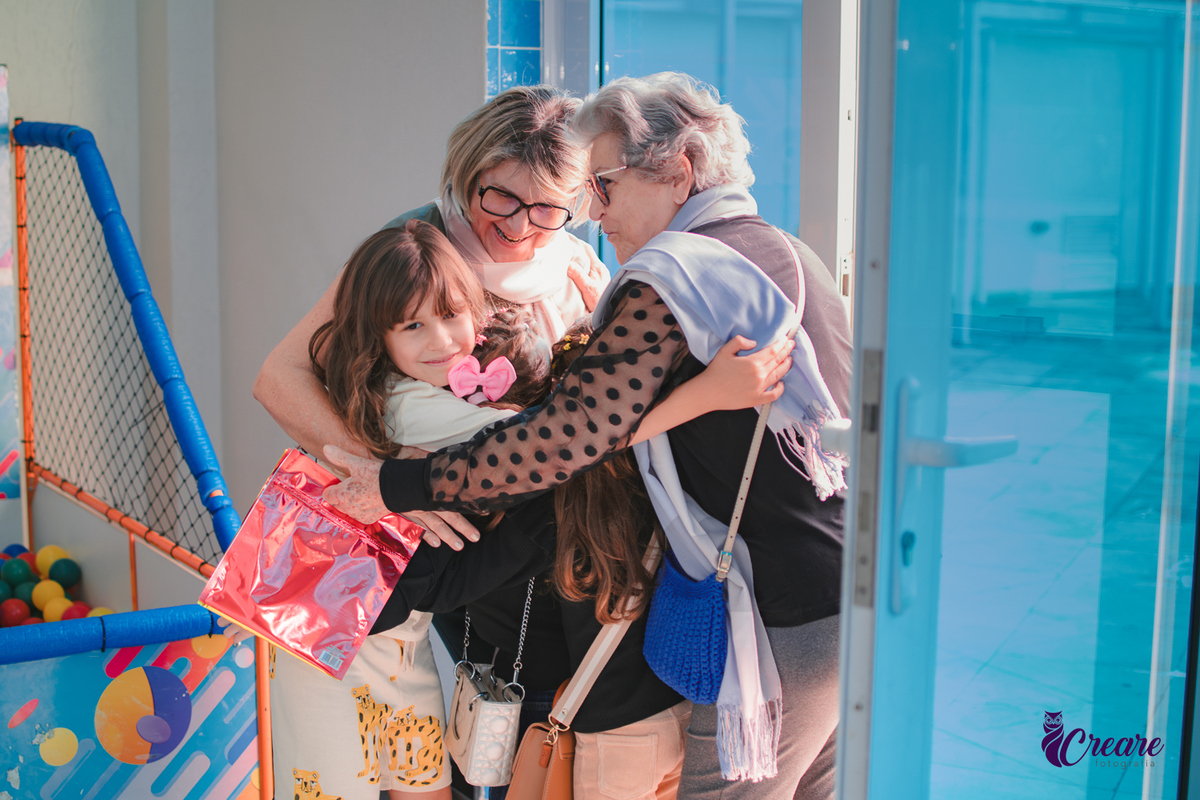crianças abraçando duas senhoras, durante aniversário infantil.