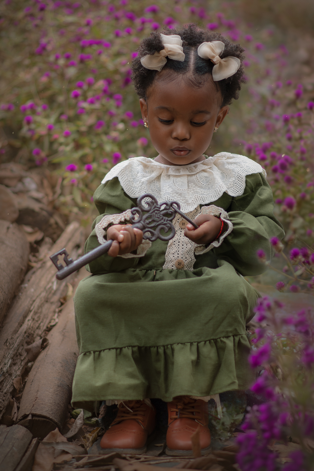Uma criança de 2anos usando vestido verde e gola branca, segurando uma chave de ferro antiga, durante seu ensaio fotográfico ao ar livre.