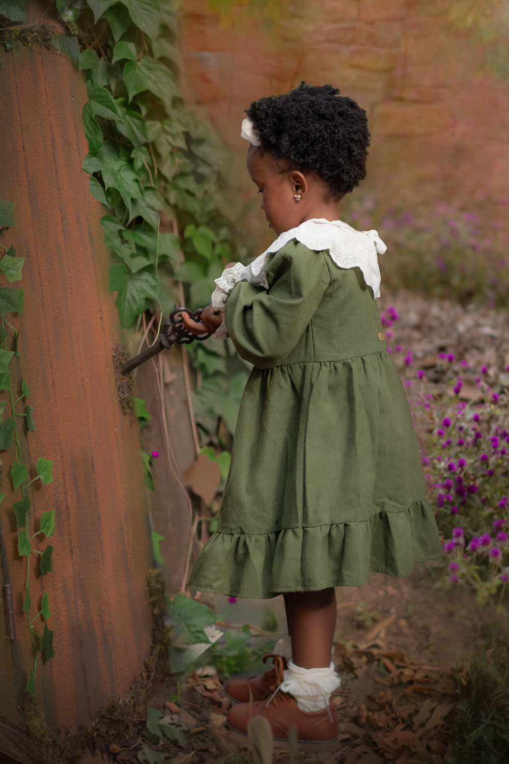 Uma criança usando vestido verde, abrindo uma porta com uma chave de ferro, durante seu ensaio fotográfico de 2 anos ao ar livre.