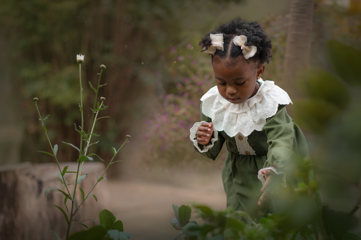 Uma criança usando vestido verde e gola branca, plantando semente de flores, durante seu ensaio fotográfico externo.