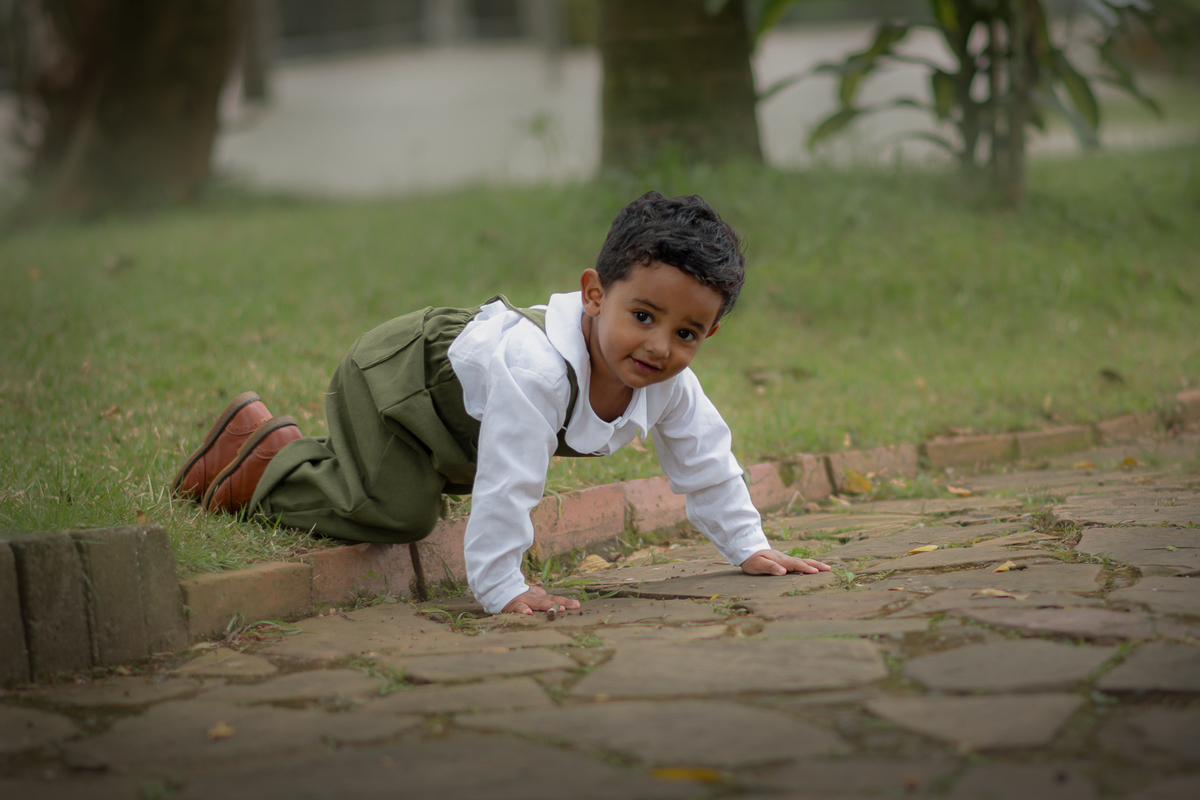 Um menino de 2 anos, engatinhando na grama e sorrindo, durante seu ensaio fotográfico no Parque Luis Carlos Grecco.