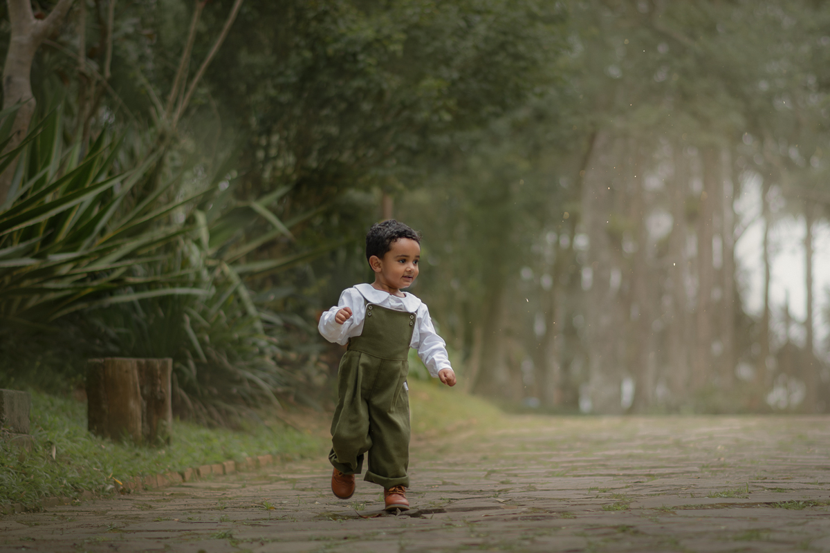 Um menino usando macacão verde e correndo no Parque Luis Carlos Grecco, durante seu ensaio fotográfico de 2 anos.