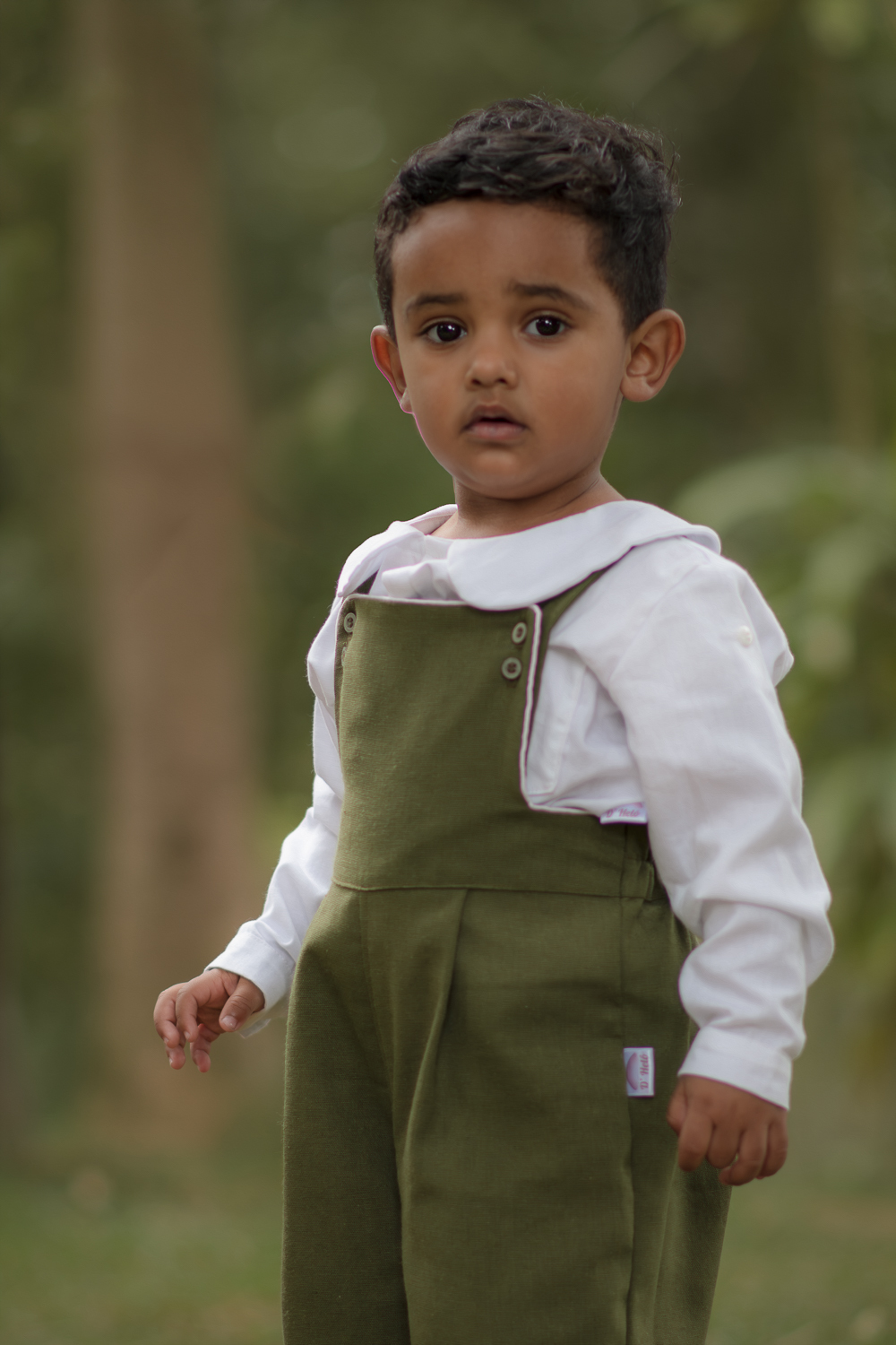 Um menino usando macacão verde e caminhando olhando paraa câmera, durante seu ensaio fotográfico de 2 anos.