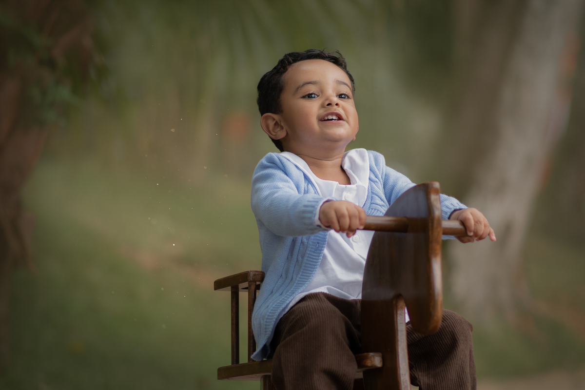 Um menino brincando de balançar em um cavalinho de madeira, durante seu ensaio fotográfico de 2 anos em Ribeirão Pires.