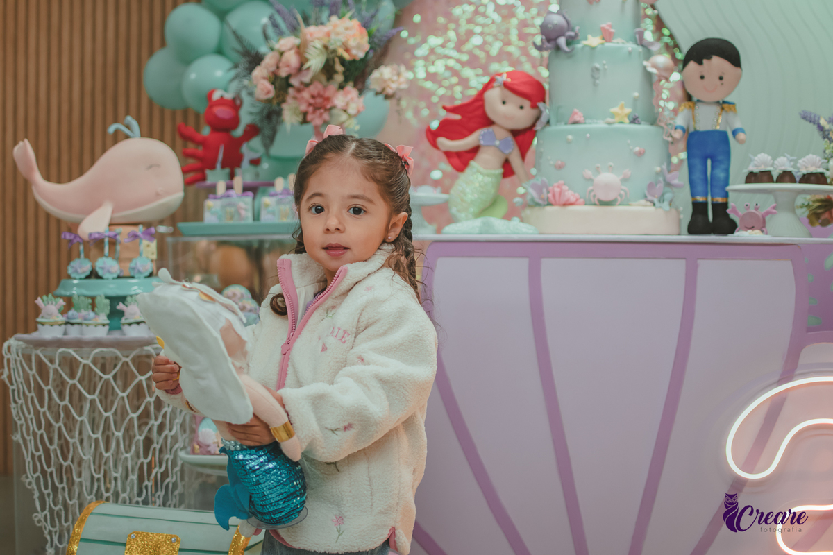 Uma criança em frente mesa de decoração com tema A pequena Sereia, durante seu aniversário de 3 anos.