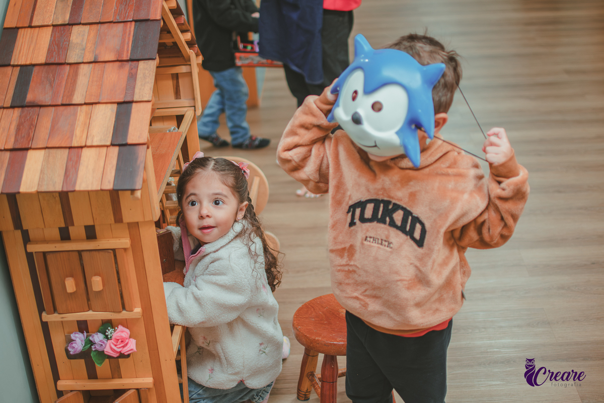 Duas crianças brincando em frente uma casinha de madeira, durante festa infantil.