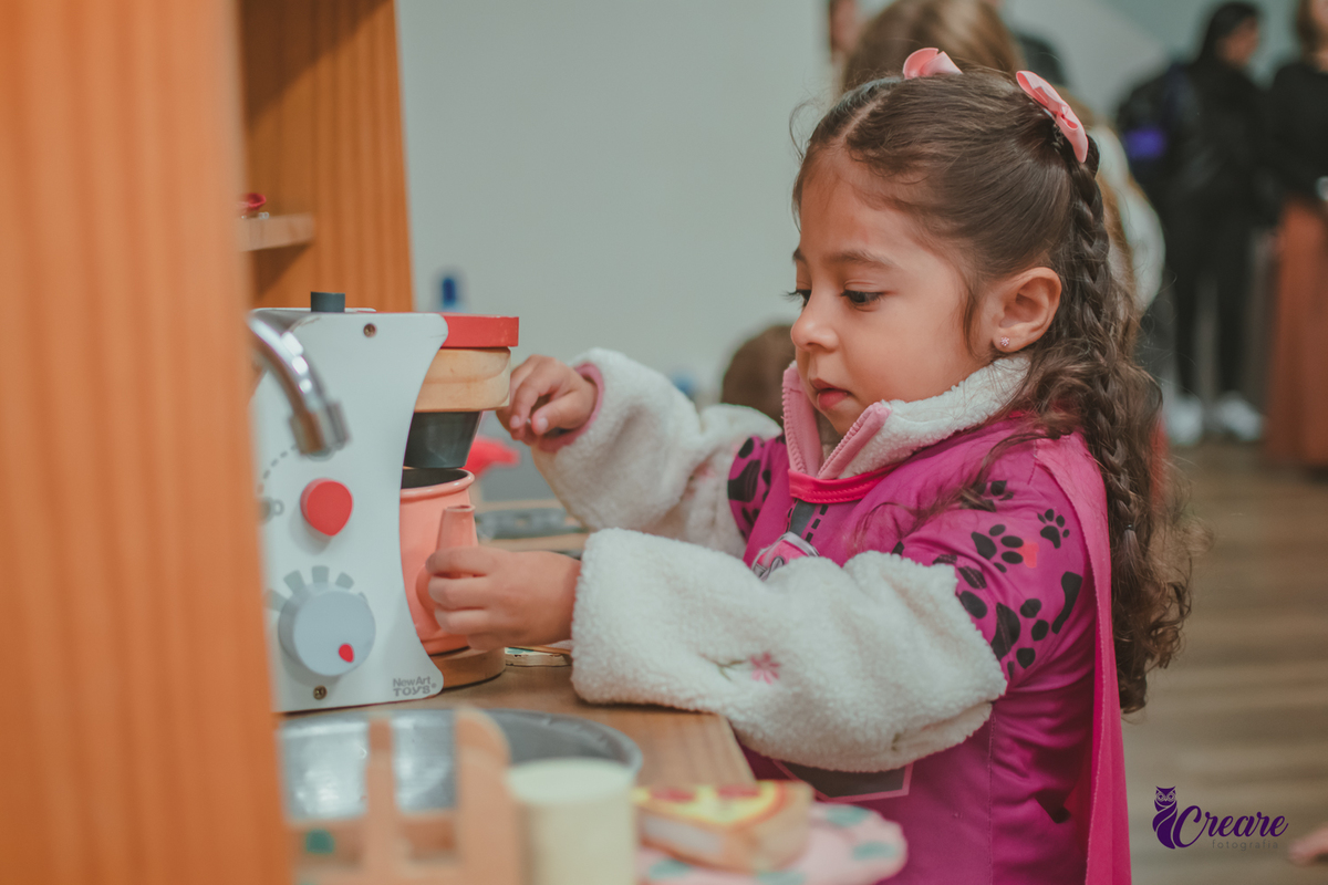 Uma criança, brincando com uma cafeteira de brinquedo, durante sua festa de aniversário.