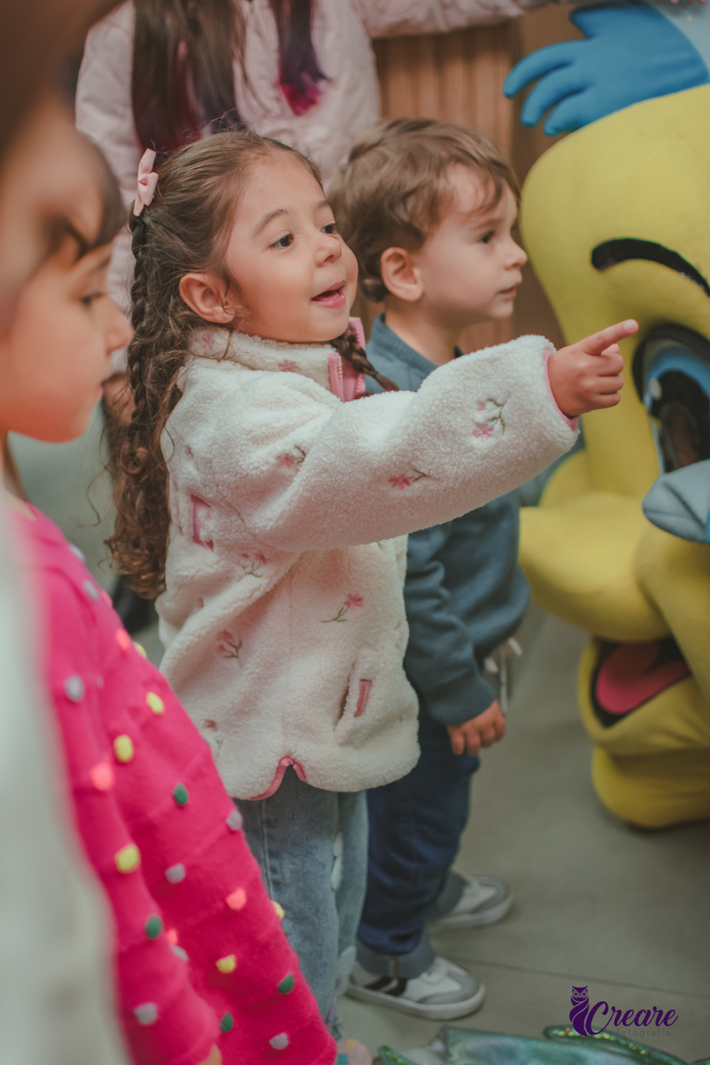 Varias crianças, pestando atenção naapresentação dos personagem de A Pequena Sereia, durante festa de aniversárui infantil.
