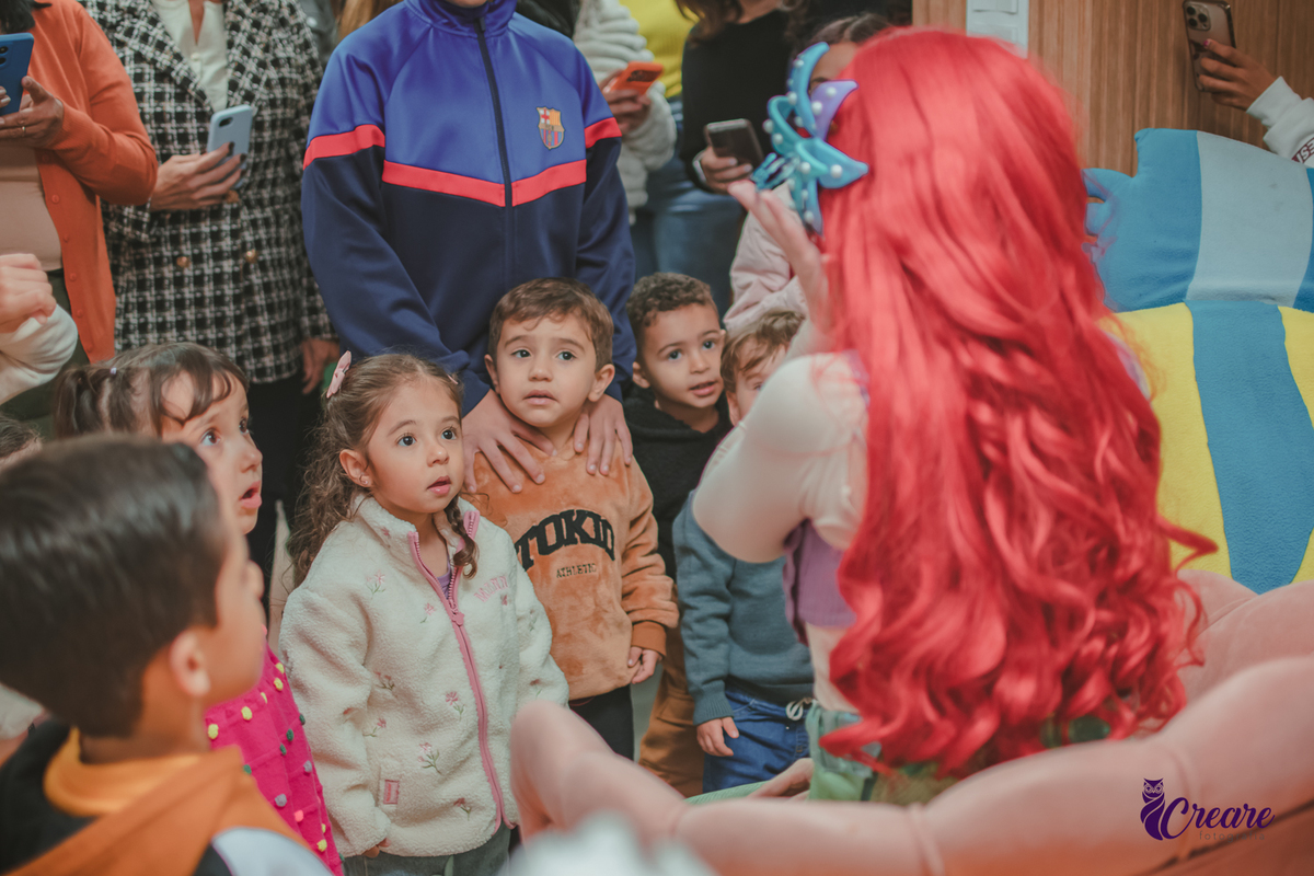 Varias crianças, pestando atenção naapresentação dos personagem de A Pequena Sereia, durante festa de aniversárui infantil.