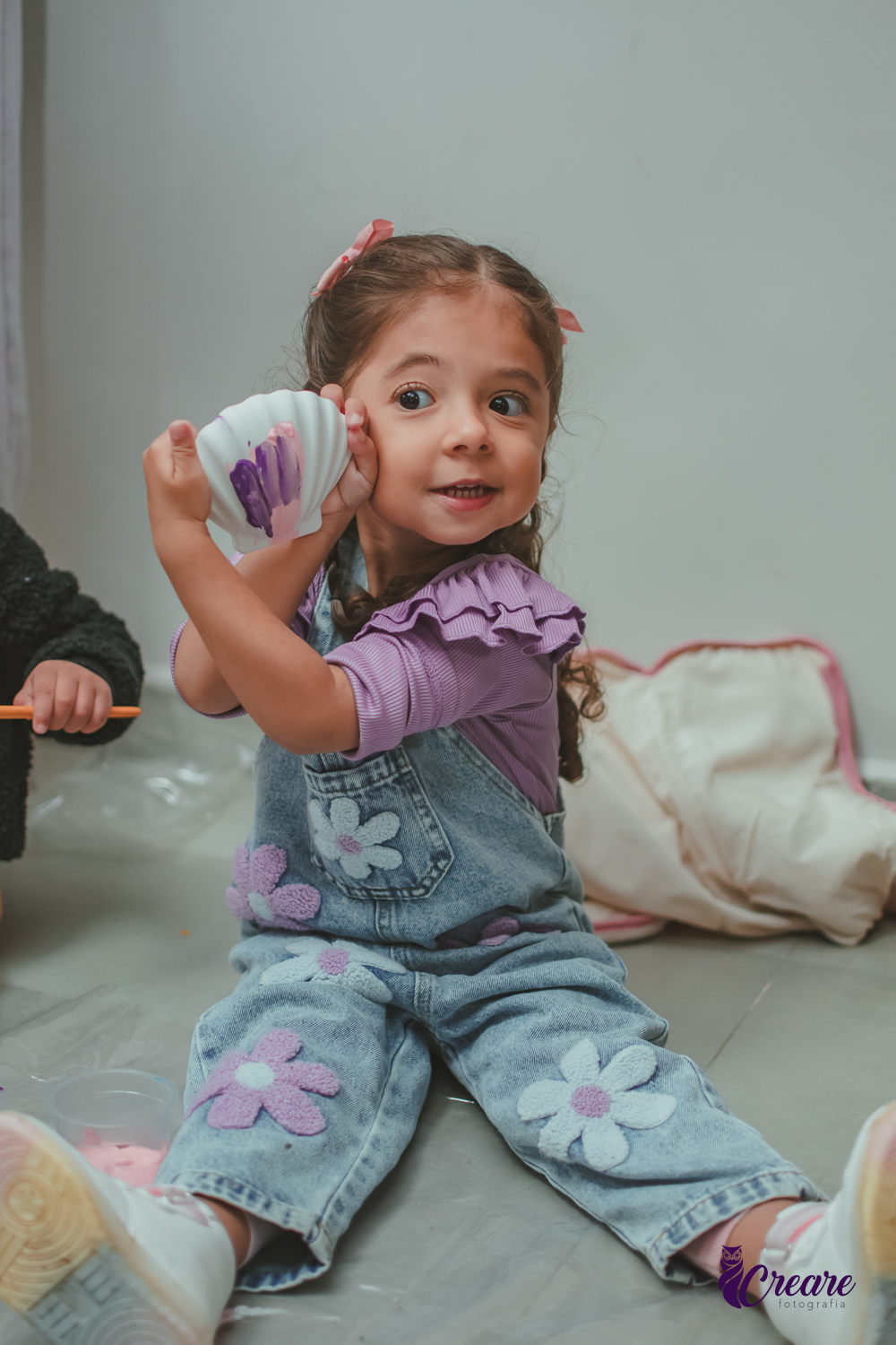 Uma criança, mostrando sua concha pintada, durante festa de aniversário de 3 anos.