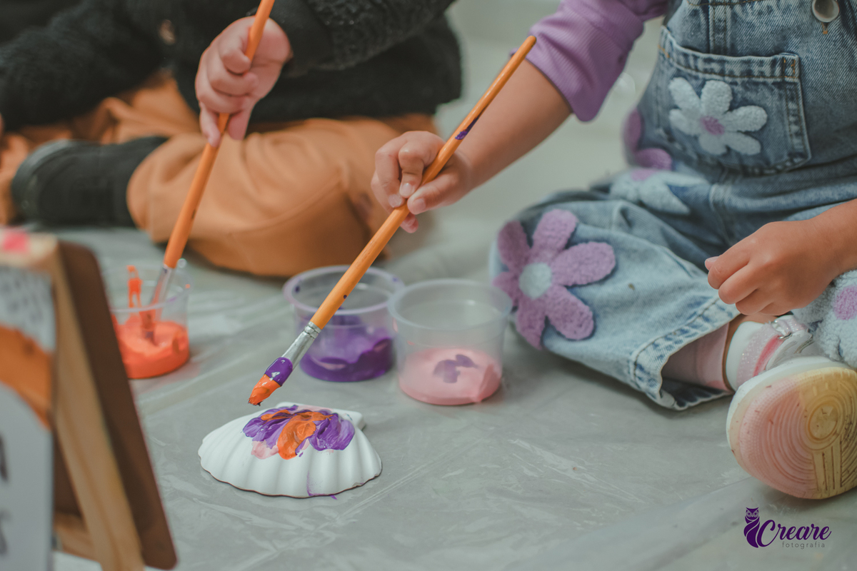Detalhes da mão de uma criança pintando uma concha de gesso, durante atividade em sua festa de aniversário.