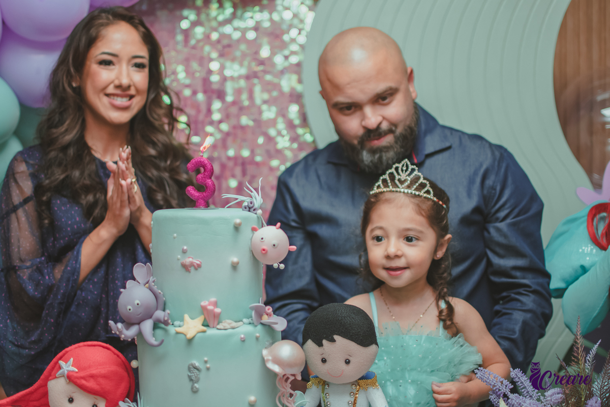 uma família e a personagem Ariel, cantando parabéns para uma criança, durante sua festa de aniversário.