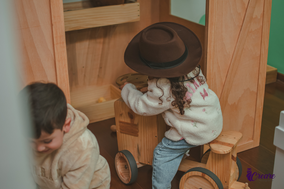 Uma criança usando chapéu de cowboy e sentando em um trato de madeira,durante sua festa de aniversário de 3 anos.