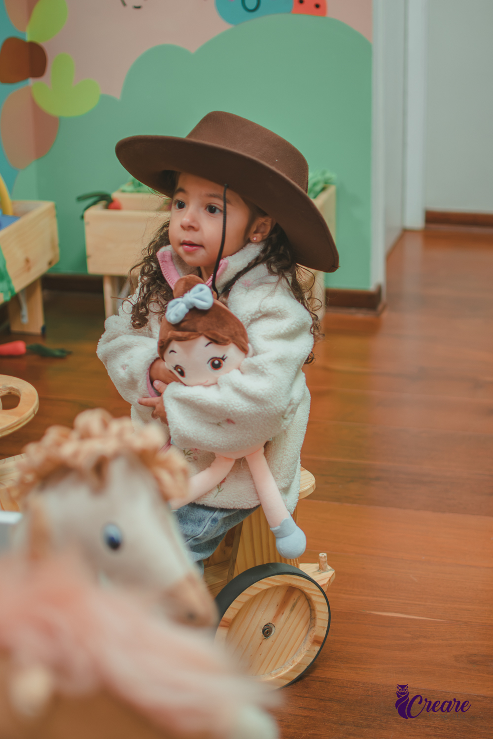 Uma criança usando chapéu de cowboy e sentando em um trato de madeira,durante sua festa de aniversário de 3 anos.