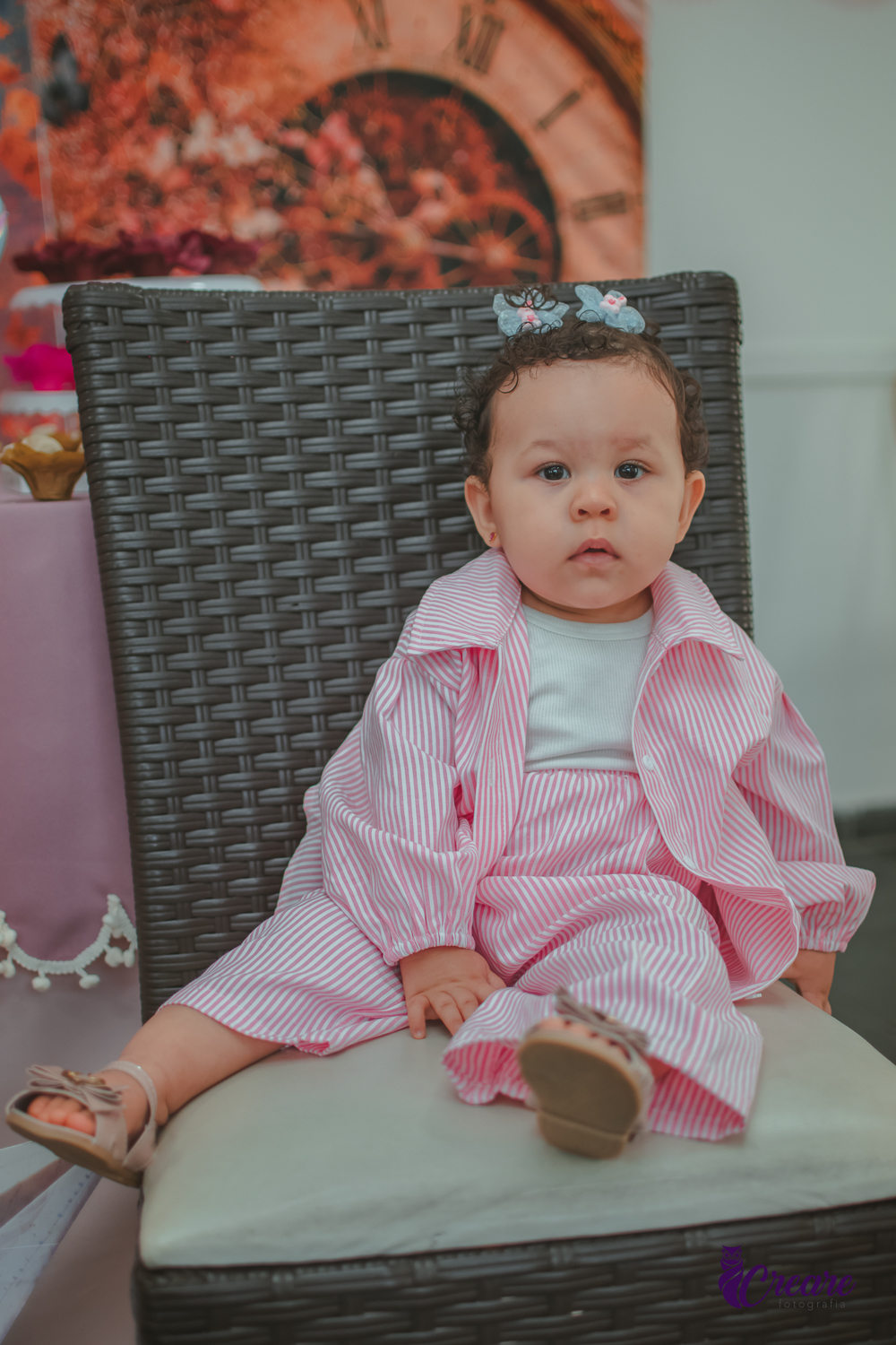 Uma menina sentada em um cadeira em frente a mesa decorada para seu aniversário de 1 ano.