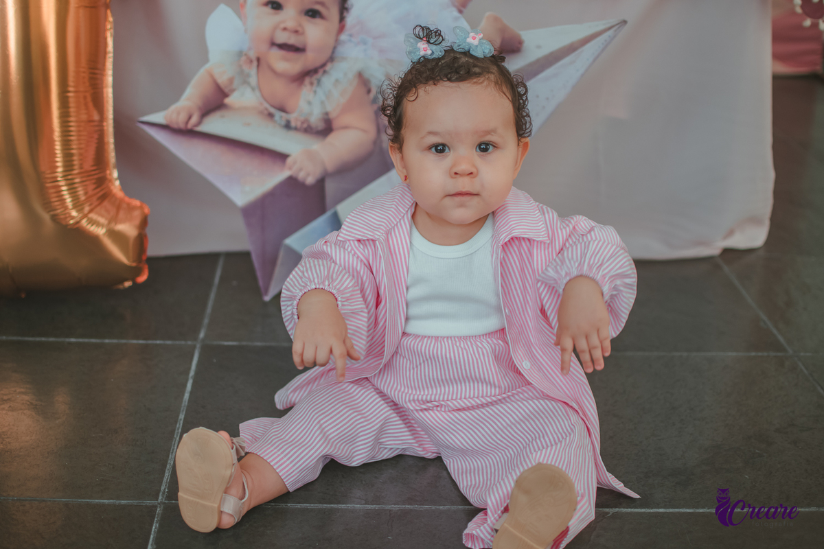 Uma menina sentada no chão, em frente um balão com número 1, durante sua festa de aniversário de um ano.