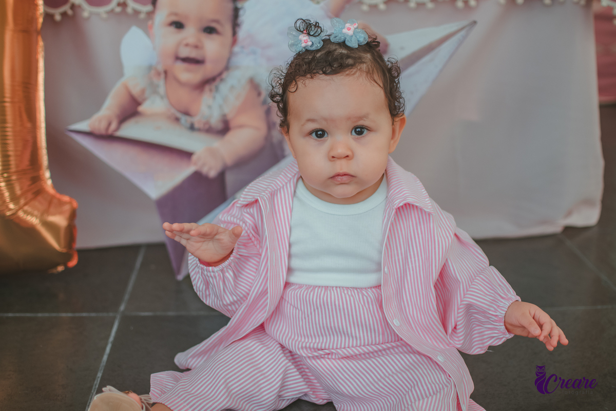 Uma menina sentada no chão, em frente um balão com número 1, durante sua festa de aniversário de um ano.