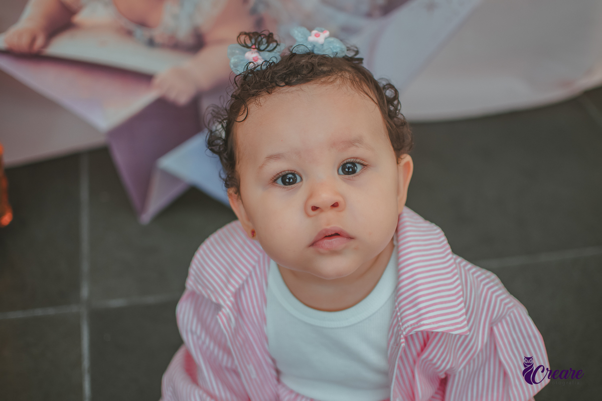 Uma menina sentada no chão, em frente um balão com número 1, durante sua festa de aniversário de um ano.