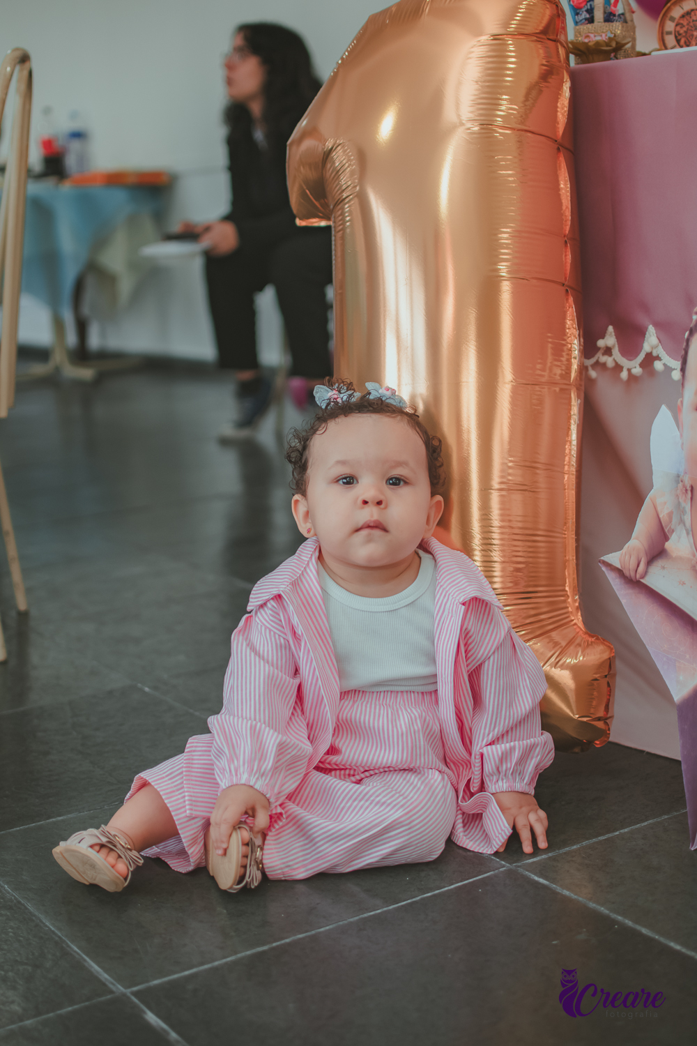 Uma menina sentada no chão, em frente um balão com número 1, durante sua festa de aniversário de um ano.