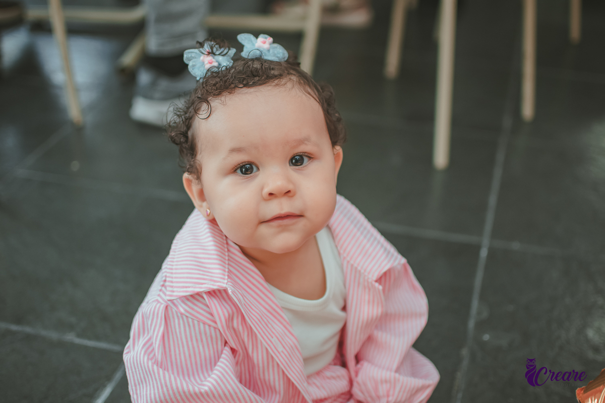 Uma menina sentada no chão e sorrindo, durante sua festa de aniversário de um ano em casa.